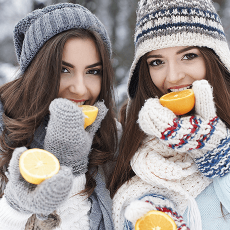 Zwei junge Frauen mit Pudelmützen beißen in Zitrusfrüchte